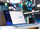 CRM software is displayed on a laptop in front of a wall of sticky notes