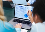 A woman points at a spreadsheet displayed on an office laptop