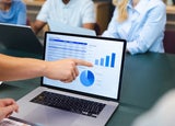 A persons hand points to a spreadsheet on a laptop screen
