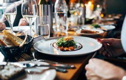 A gourmet meal on a white plate is set in front of a patron in a restaurant