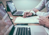 Two colleagues complete paperwork in front of their laptops