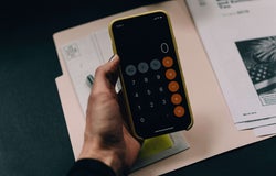 A hand holds a smartphone with a the calculator app open.