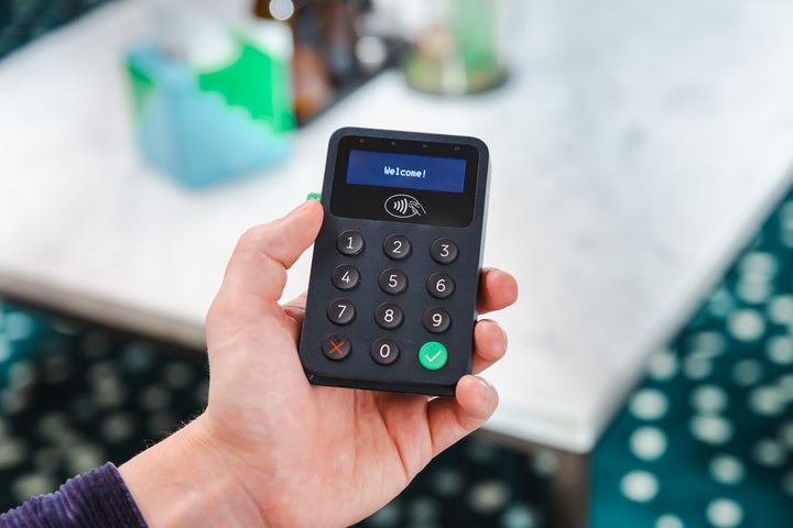 A hand holding a small, black card machine reader with the display reading 'welcome'